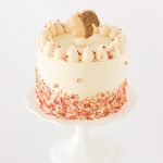 Three-layer pumpkin spice cake with maple caramel buttercream, topped with fall sprinkles and a sugar cookie squirrel, perfect for Thanksgiving celebrations