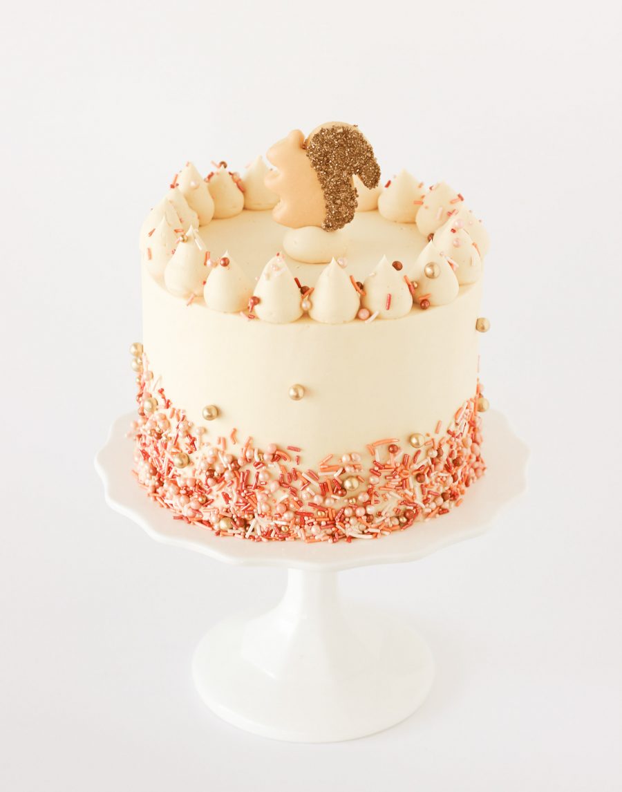 Three-layer pumpkin spice cake with maple caramel buttercream, topped with fall sprinkles and a sugar cookie squirrel, perfect for Thanksgiving celebrations
