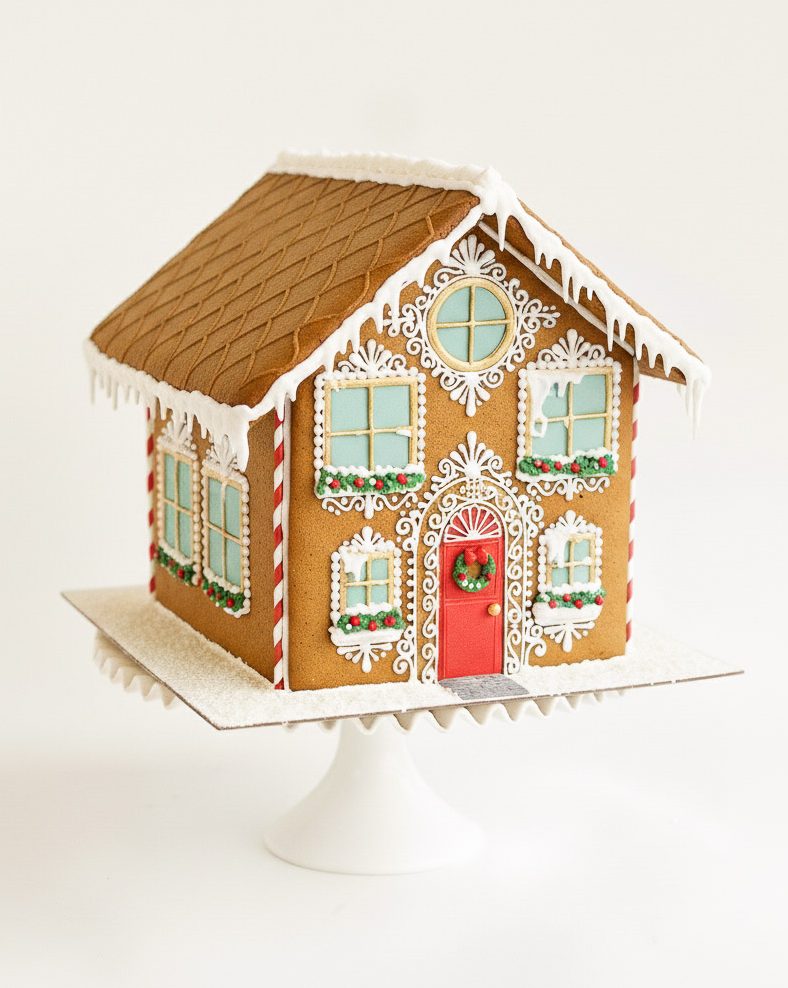 Elaborately decorated gingerbread house with red door, candy canes, and white royal icing